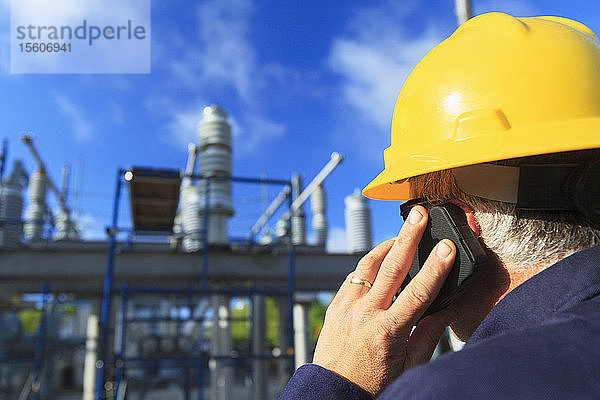 Energietechniker  der in einer Hochspannungsverteilerstation mit einem Mobiltelefon spricht