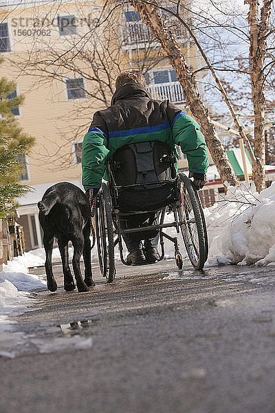 Frau mit Multipler Sklerose in einem Rollstuhl mit einem Diensthund im Winter