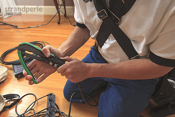 Kabelinstallateur  der mit einer Crimpzange einen neuen Kabelstecker an ein Kabel anbringt