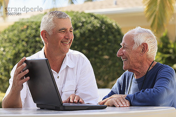 Ein älterer Mann zeigt seinem sehbehinderten Vater lächelnd einen Laptop