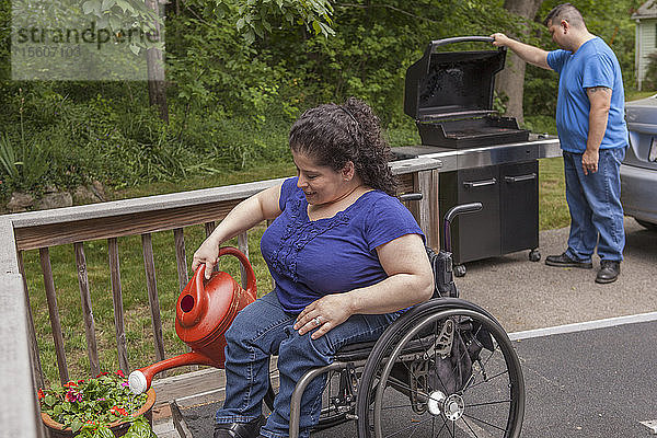 Frau mit Spina Bifida gießt ihre Blumen mit ihrem Mann im Hintergrund