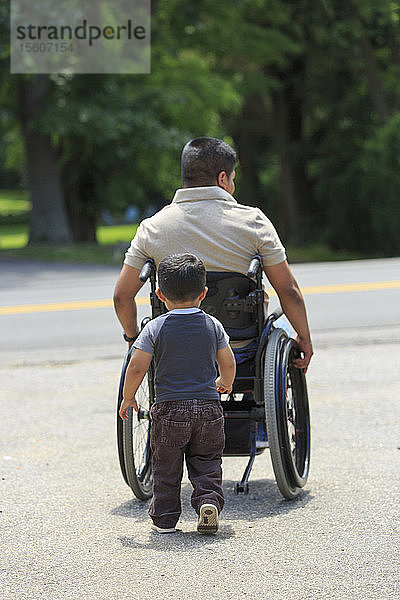 Hispanoamerikanischer Mann mit Rückenmarksverletzung im Rollstuhl mit seinem Sohn