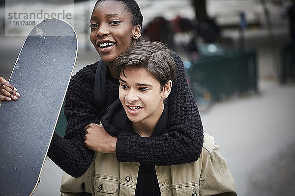 Junger Mann fährt mit Skateboard Huckepack mit einer Teenager-Freundin