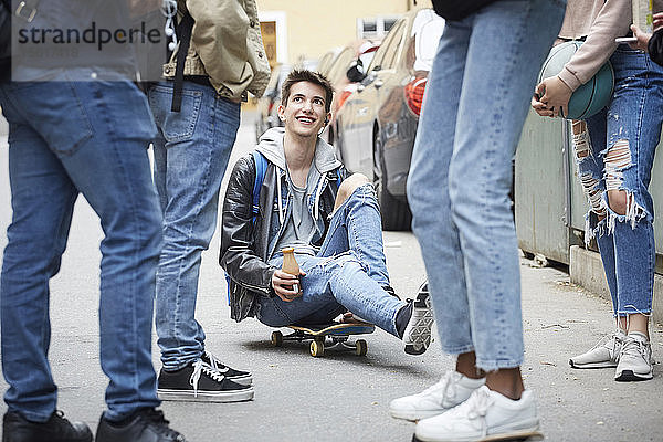 Niedrige Sektion von Freunden steht neben einem lächelnden Teenager  der auf einem Skateboard sitzt