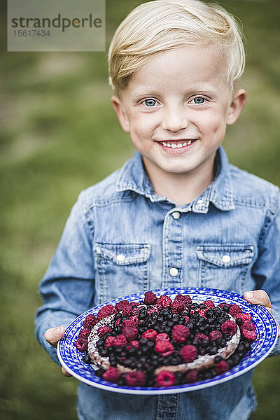 Porträt eines lächelnden Jungen mit Beerentorte im Garten