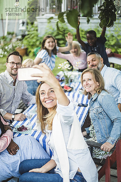 Frau nimmt sich mit Familie und Freunden am Esstisch bei Gartenparty