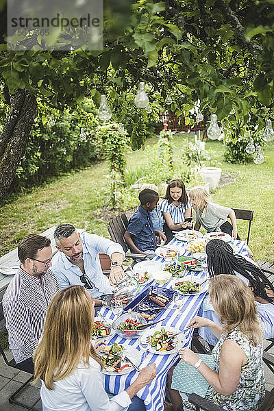 Schrägaufnahme von Freunden und Familie am Esstisch bei einer Gartenparty