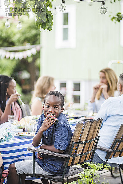 Lächelnder Junge isst Wassermelone  während er mit der Familie in der Gartenparty sitzt