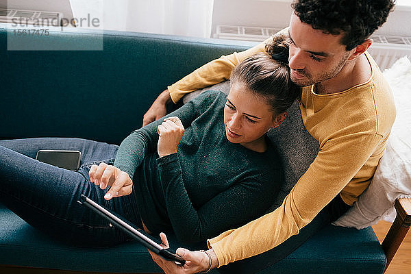 Freund und Freundin benutzen ein digitales Tablet  während sie sich zu Hause auf dem Sofa entspannen