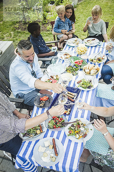 Freunde und Familie stoßen beim Mittagessen im Garten auf Weingläser an