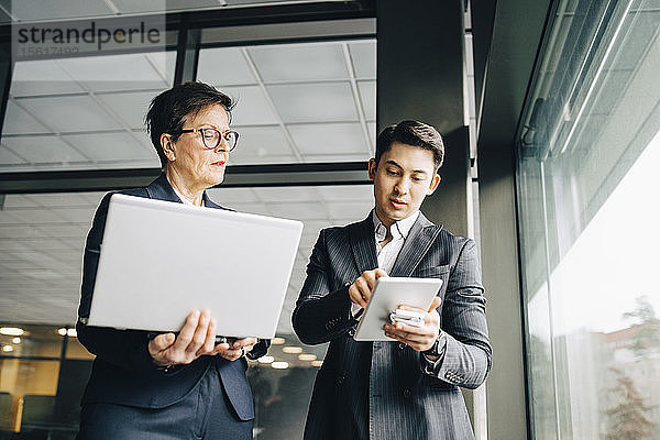 Männlicher leitender Angestellter zeigt im Amt stehend einem leitenden Angestellten ein digitales Tablet