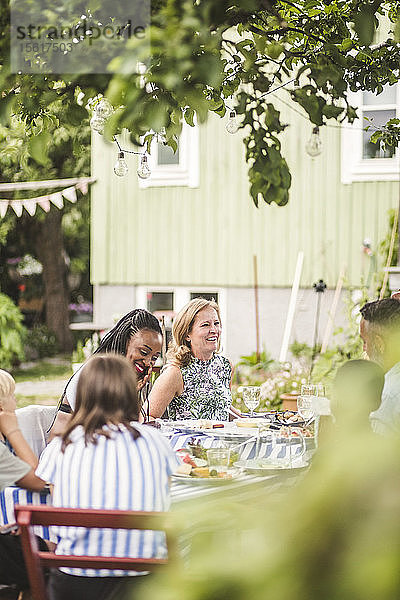 Familie und Freunde genießen das Essen  während sie im Hinterhof zusammen am Tisch sitzen