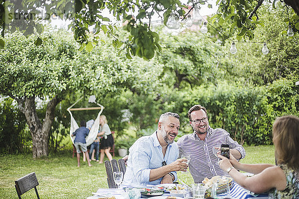 Frau mit Handy fotografiert männliche Freunde beim Trinken auf Gartenparty