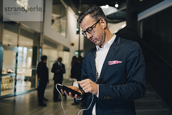 Geschäftsmann benutzt Smartphone  während er im Büro über Kopfhörer hört