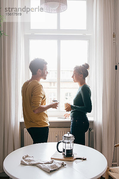 Seitenansicht eines Paares  das sich unterhält  während es zu Hause am Fenster steht