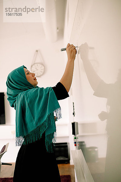 Seitenansicht einer Geschäftsfrau in Hijab-Schrift an der Tafel im Kongresszentrum