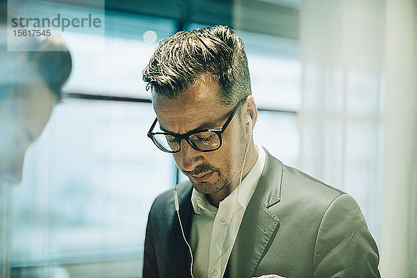 Nachdenklicher männlicher Profi mit Brille und Kopfhörer im Büro