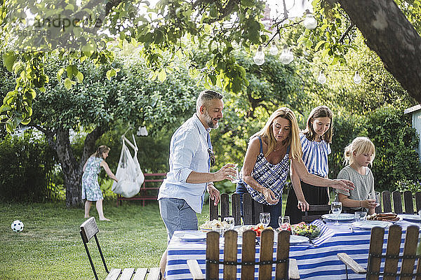 Familie arrangiert Essen auf dem Tisch für geselliges Beisammensein am Sommerwochenende