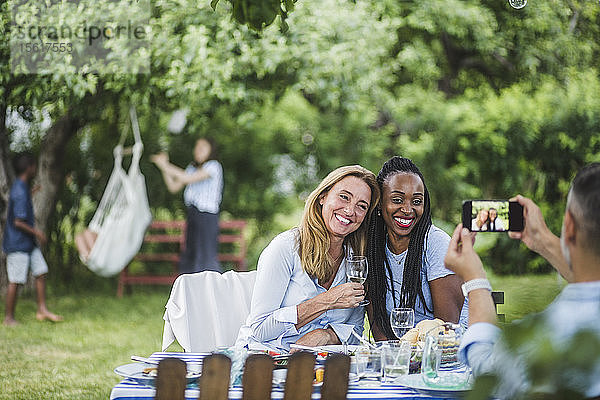 Mann fotografiert Freunde mit Wein über Handy auf Gartenparty
