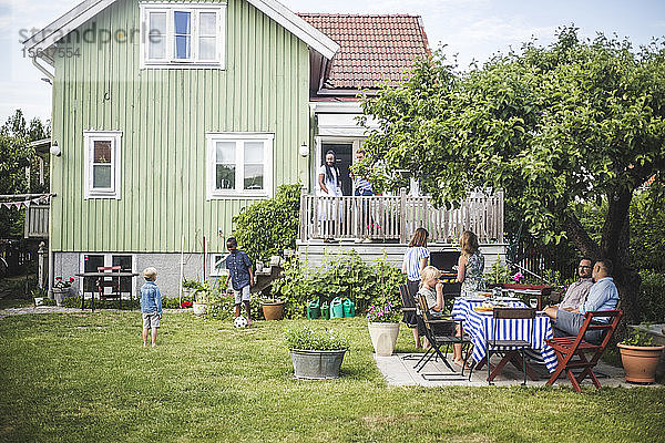 Reife Freunde feiern am Sommerwochenende eine Gartenparty  während Kinder im Garten spielen