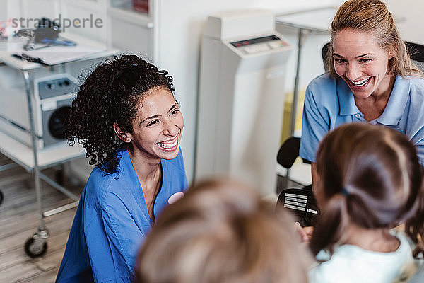 Hochwinkelansicht eines lächelnden Kinderarztes und einer Krankenschwester  die sich mit einem Mädchen im Untersuchungszimmer unterhalten