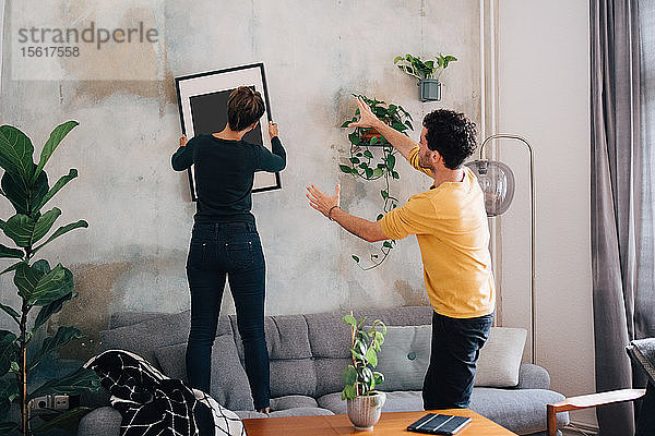 Mittelgroßer erwachsener Mann führt Freundin im hängenden Bilderrahmen an der Wand im neuen Zuhause