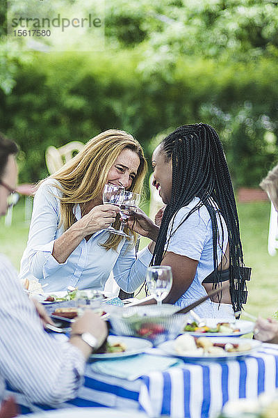 Glückliche Freundinnen stoßen während der Gartenparty am Esstisch auf Weingläser an