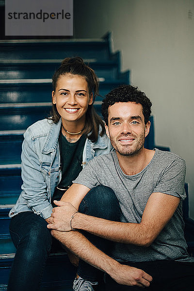 Porträt eines lächelnden Paares  das auf Stufen in einer Wohnung sitzt