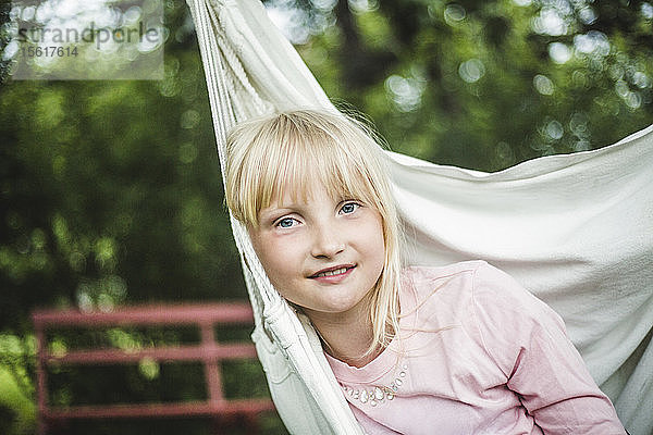 Porträt eines lächelnden Mädchens  das in einer weißen Schaukel im Garten sitzt