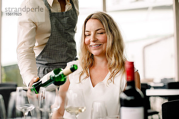 Geschäftsmann serviert einer lächelnden Kollegin im Kongresszentrum Wein