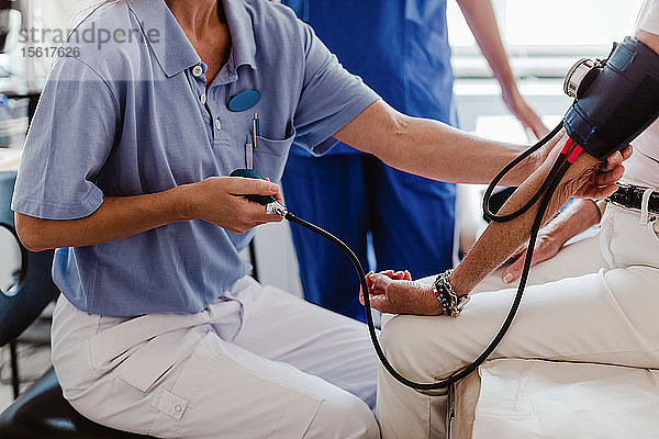 Mittelsektion einer Ärztin  die den Blutdruck einer älteren Patientin im Behandlungszimmer überprüft