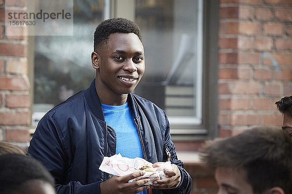 Porträt eines lächelnden Teenagers  der Essen hält  während er im Freien steht