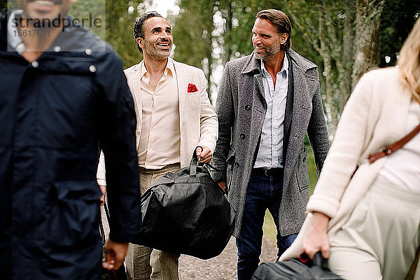 Lächelnde männliche Berufstätige  die während einer Geschäftsreise mit Kollegen gehen