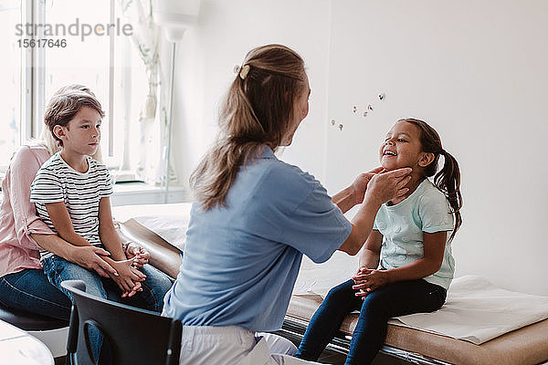 Weibliche Ärztin untersucht lächelndes Mädchen  während die Familie im Behandlungszimmer sitzt