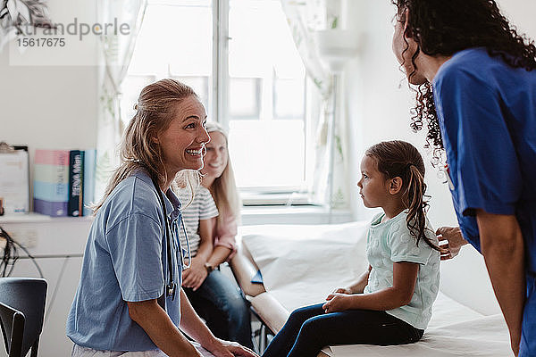 Fröhliche Kinderärztin im Gespräch mit Krankenschwester bei Untersuchung eines Mädchens in medizinischer Klinik