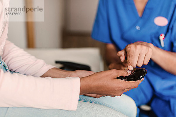 Mittelsektion einer Krankenschwester und einer Patientin beim Ablesen des Zuckerspiegels von medizinischen Geräten in der Klinik