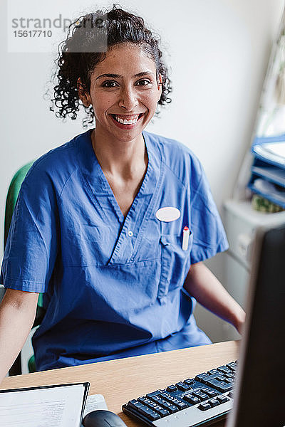 Porträt einer lächelnden Krankenschwester  die im Krankenhaus am Schreibtisch sitzt