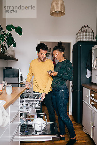 Frau zeigt ihrem Freund ein Handy  während sie in der Küche steht