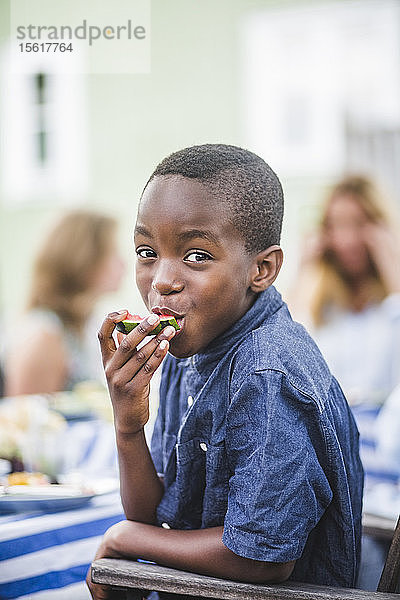 Porträt eines lächelnden Jungen  der auf einer Party im Garten eine Wassermelone isst