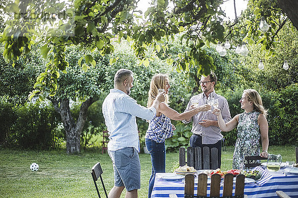 Glückliche Freunde klimpern beim Weinglas  während sie während der Wochenendparty im Hinterhof stehen