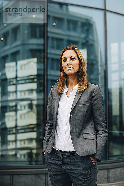 Porträt einer selbstbewussten Geschäftsfrau  die sich gegen die Reflexion über ein Glasgebäude stellt