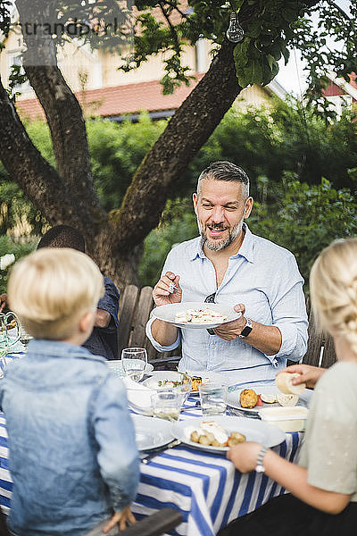 Reifer Mann spricht  während er Kindern auf einer Party einen Speiseteller zeigt