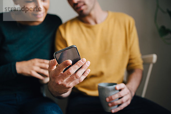 Mitschnitt eines Freundes  der seiner Freundin beim Kaffee zu Hause ein Smartphone zeigt