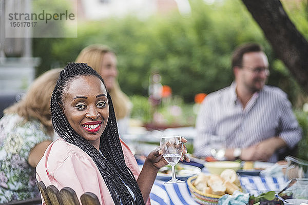 Porträt einer lächelnden Frau  die Wein trinkt  während sie mit Freunden auf einer Gartenparty sitzt