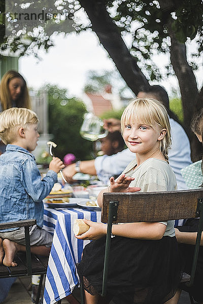 Porträt eines lächelnden Mädchens  das mit Freunden und Familie bei Tisch in einer Gartenparty sitzt