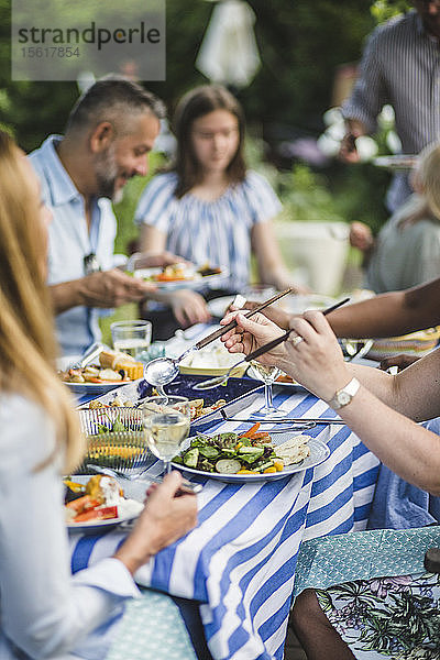 Frau serviert Essen  während sie während einer Wochenendparty mit Freunden und Familie im Hinterhof sitzt