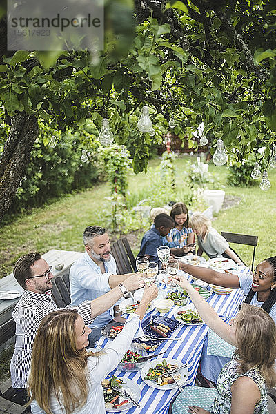Schrägansicht von Freunden  die während einer Gartenparty im Sommer auf Weingläser anstoßen