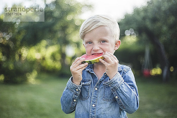 Porträt eines Jungen  der im Hinterhof frische Wassermelone isst