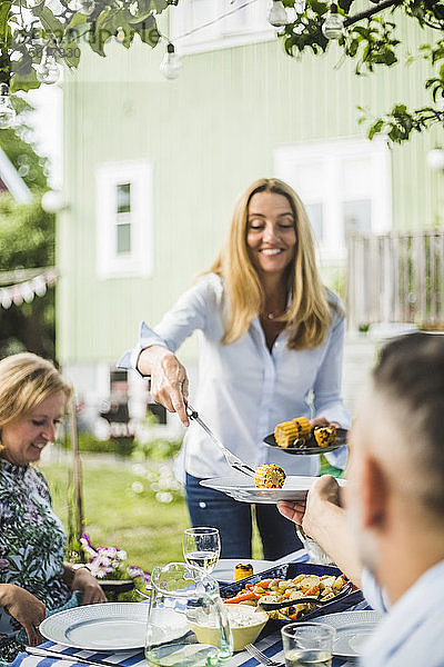Frau serviert gegrillte Hühneraugen für Freunde am Esstisch bei einer Gartenparty