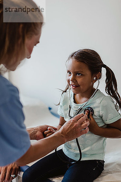 Lächelndes medizinisches Personal unterstützt Mädchen beim Abhören ihrer eigenen Herzschläge im Krankenhaus
